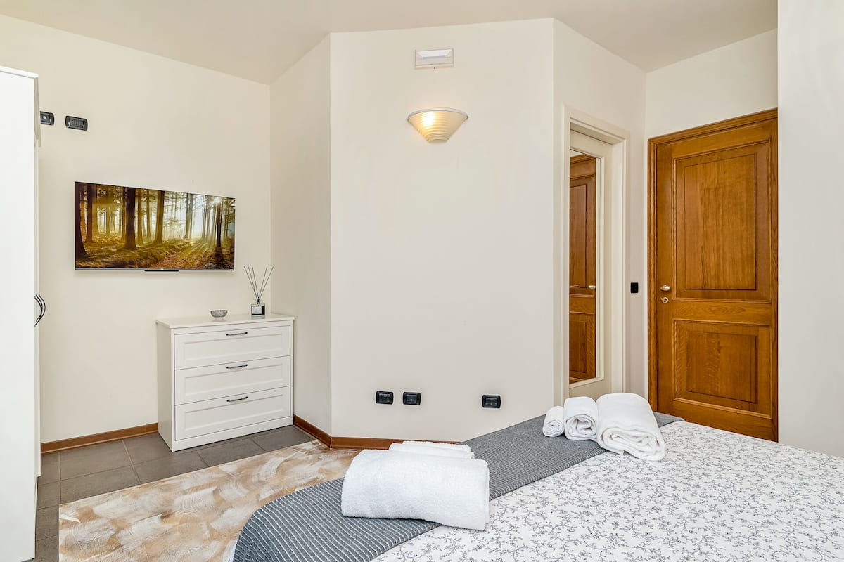 Une chambre à coucher avec un lit, une commode, un tableau, un luminaire et une porte en bois.