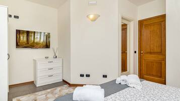 Een slaapkamer met een bed, een dressoir, een schilderij, een lamp en een houten deur.