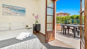 A bedroom with a bed, a nightstand, a painting, a potted plant, and a sliding glass door leading to an outdoor area with a table and chairs. - Hotel la Pietra Restaurant (Fosdinovo)