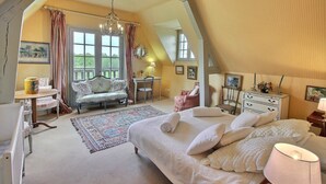 Een knus slaapkamer met een groot bed, een zithoek met een bank en fauteuil, een eettafel en een kroonluchter.