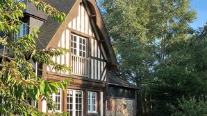 Een traditioneel vakwerkhuis met een stenen muur, een houten deur en een kleine tuin met plantenbakken en terrasmeubels.