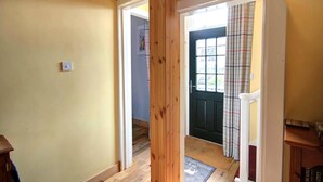 A hallway with a wooden door leading to a room with a black door and plaid curtains. - Red Brick Former Railway Workers' Cottage (Brora)