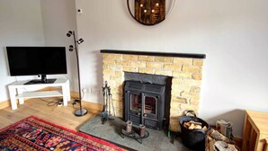 A living room with a fireplace, a television, and a rug. - Red Brick Former Railway Workers' Cottage (Brora)