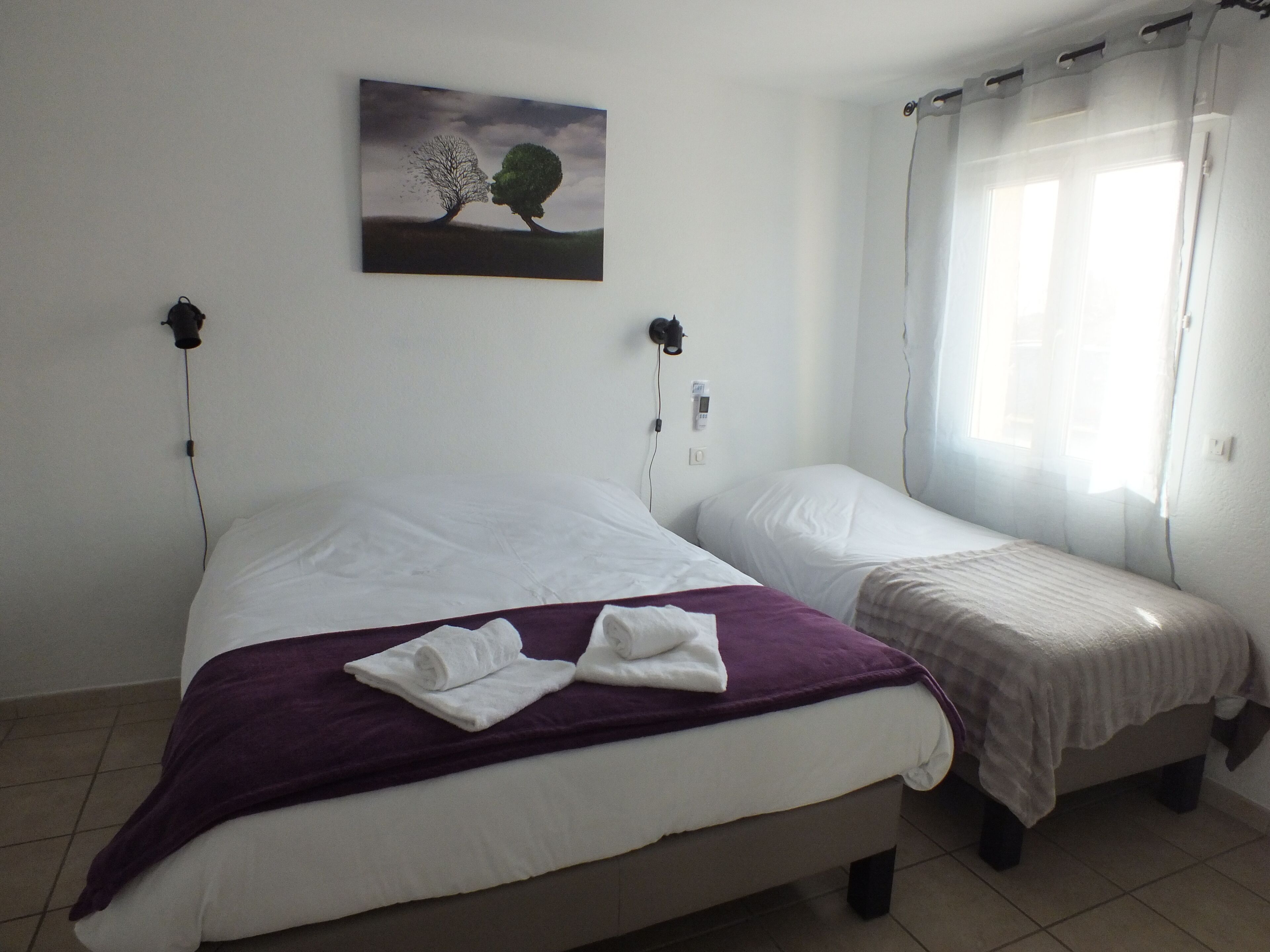 A bedroom with two beds, a painting on the wall, and a window with curtains.