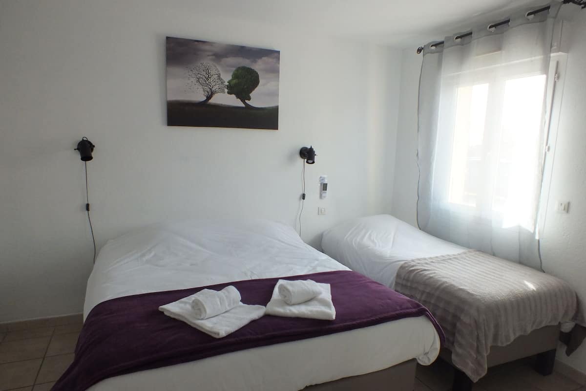 A bedroom with two beds, a painting on the wall, and a window with curtains.