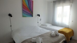 A room with two beds, a colorful abstract painting, a window with curtains, and a towel on the bed. - Logis Hôtel le Clos Saint-Loup (Bram)