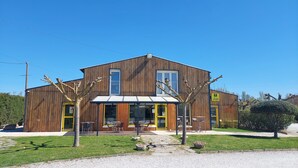 A modern two-story building with a wooden facade, large windows, and outdoor seating area. - Logis Hôtel le Clos Saint-Loup (Bram)