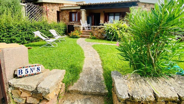 Una casa de piedra con un sendero empedrado que conduce a un porche con dos sillas blancas.
