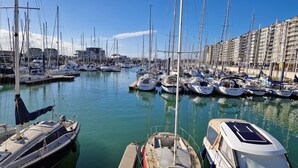 Un port de plaisance où sont amarrés de nombreux bateaux, un bâtiment en arrière-plan et un ciel dégagé.