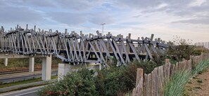 Un pont en bois, doté de garde-corps métalliques et reposant sur une base en béton, enjambant une route protégée par une glissière de sécurité.