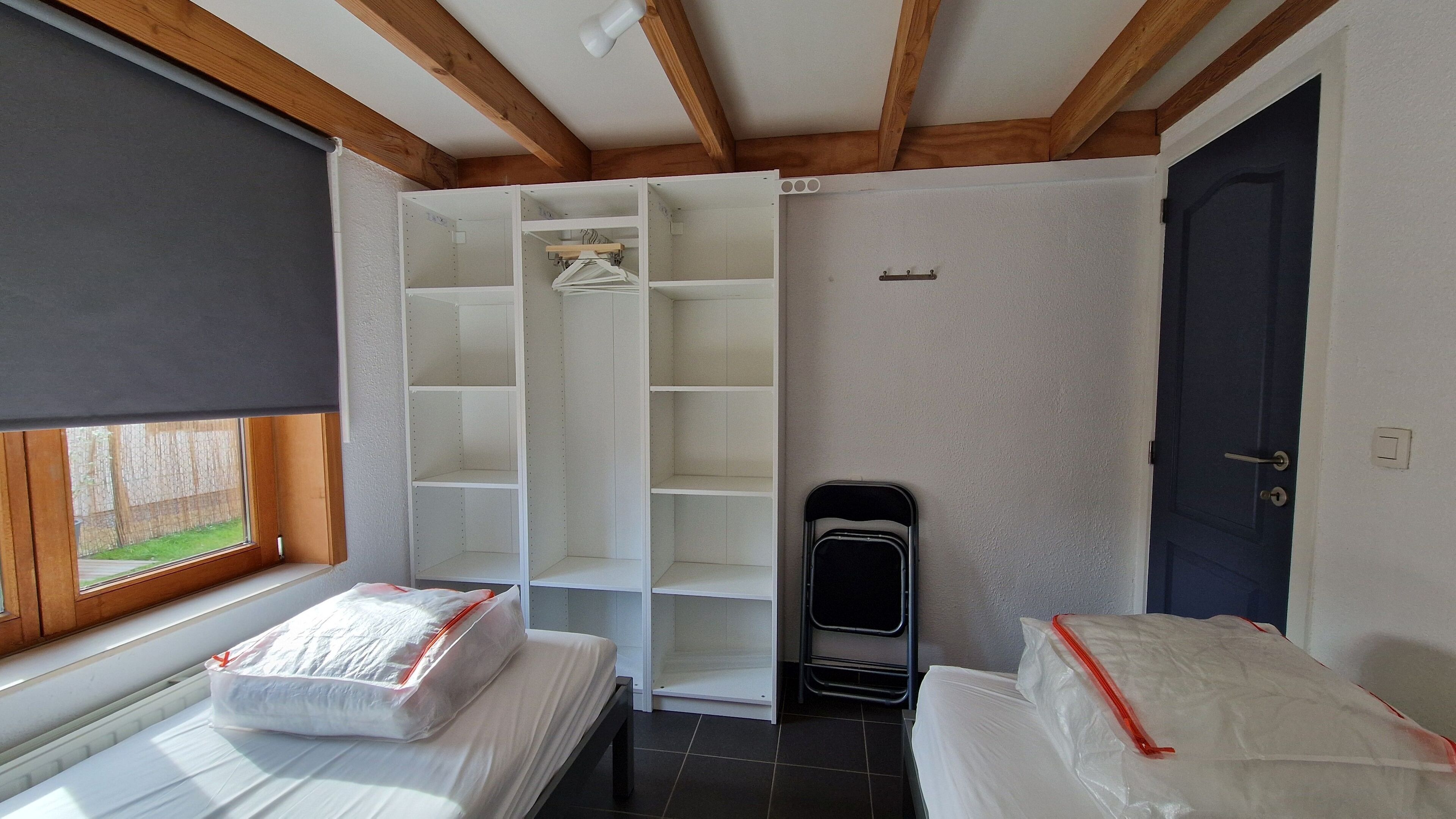 A bedroom with a bed, a wardrobe, a radiator, and a window with a view of a fence.