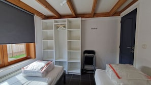 Et soveværelse med seng, garderobeskab, radiator og et vindue med udsigt til et hegn.
