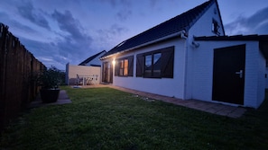 A white house with a dark roof, a wooden fence, and a grassy yard. - Fisherman's cottage in Wenduine, close to the beach and marina of Blankenberge. (De Haan)