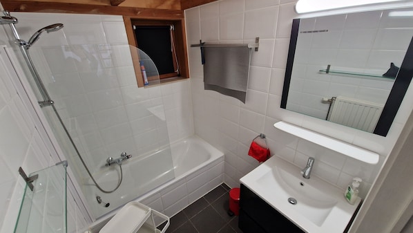 Ein Badezimmer mit einer Glaskabine für die Dusche, einer Badewanne, einem Waschbecken und einem Spiegel.