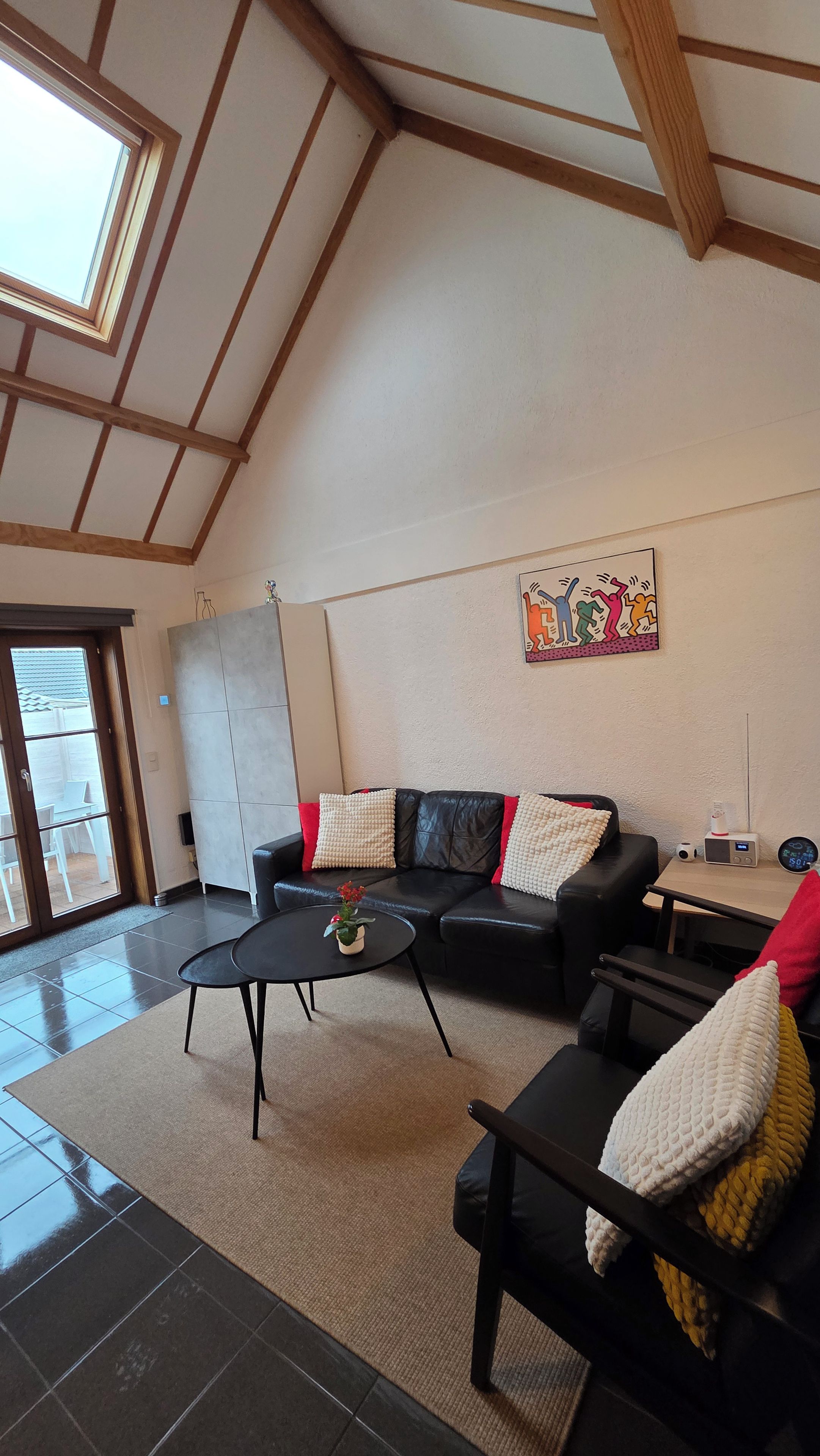 A living room with a black leather sofa, a coffee table, and a painting on the wall.