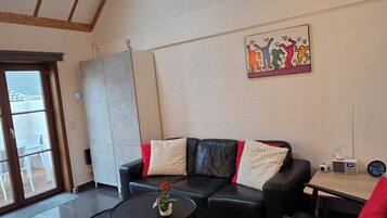 A living room with a black leather sofa, a coffee table, and a painting on the wall.