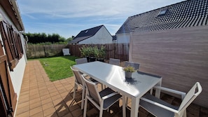 Eine Terrasse mit weißem Tisch und Stühlen, einem kleinen Topfpflanzen und einem Holzzaun im Hintergrund.