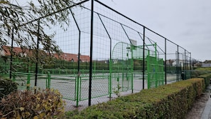 Ein eingezäuntes Sportgelände mit grünen Metallkonstruktionen und einer Hecke entlang der Seite.