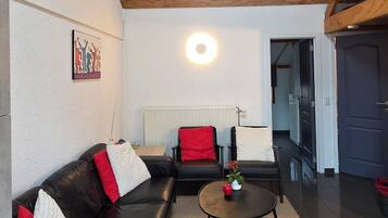 A modern living room with a black leather sofa, a round coffee table, and a red and white pillow.