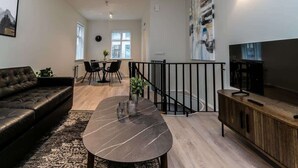 A modern living room with a leather sofa, a marble coffee table, a TV, and a dining area with a table and chairs.
