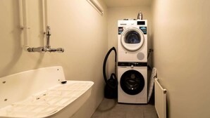 A compact bathroom with a bathtub, a stacked washer and dryer, and a visible pipe.