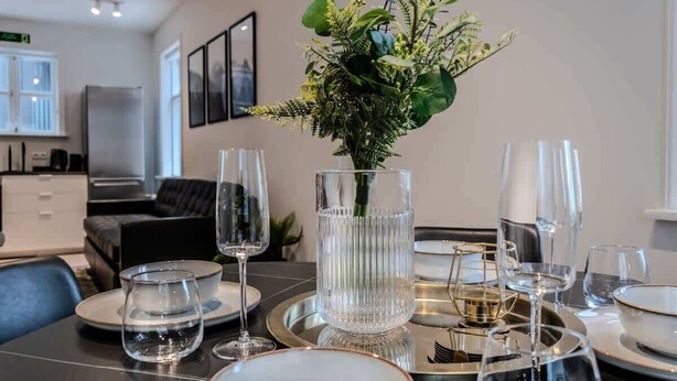 A dining table set with clear glassware and a centerpiece of greenery.