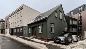 A residential street with houses, one with a sloped roof and a parked car.