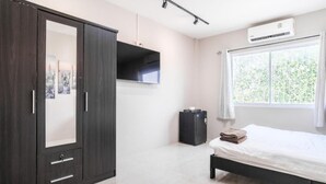 Ein Schlafzimmer mit Bett, Kleiderschrank, Flachbildfernseher, einem Fenster mit Vorhängen und einem kleinen Tisch mit Wasserkocher.