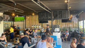 Ein Restaurant im Freien mit blauen Sitzplätzen, einer Bar und einem Sportbildschirm.