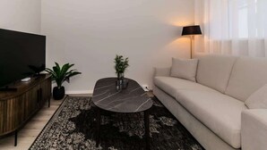 Una sala moderna con un sofá, una televisión, una mesa de centro, una lámpara y una planta.