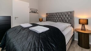 Un dormitorio con una cama, dos mesitas de noche, una puerta y un perchero en la pared.