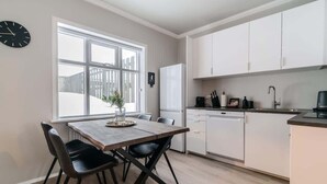 Una cocina moderna con armarios blancos, una mesa de comedor con sillas, un reloj y un ventanal con vistas.