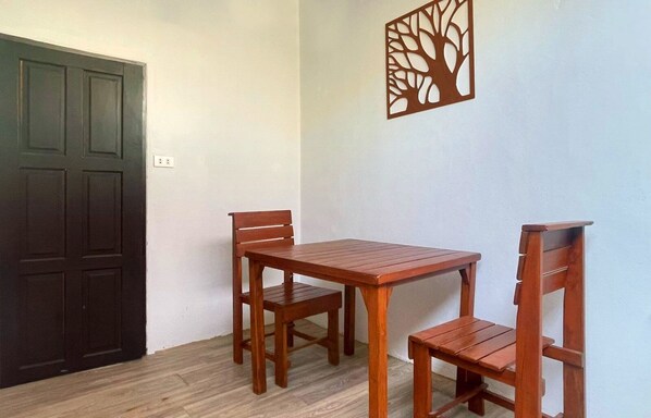 A room with a wooden table and two chairs, a dark door, and a wall decoration. - New Breakers Hotel Rawai (Rawai)