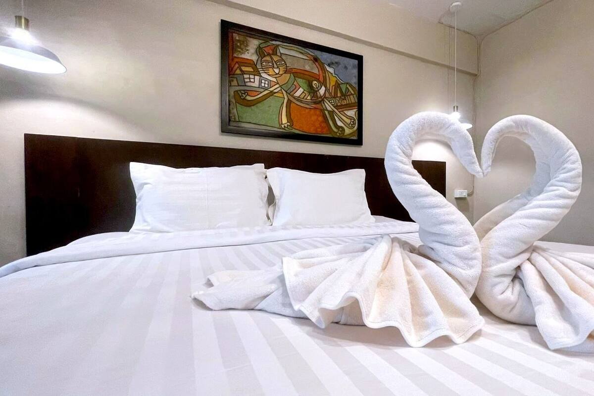 A hotel room with a bed, pillows, and a painting on the wall.