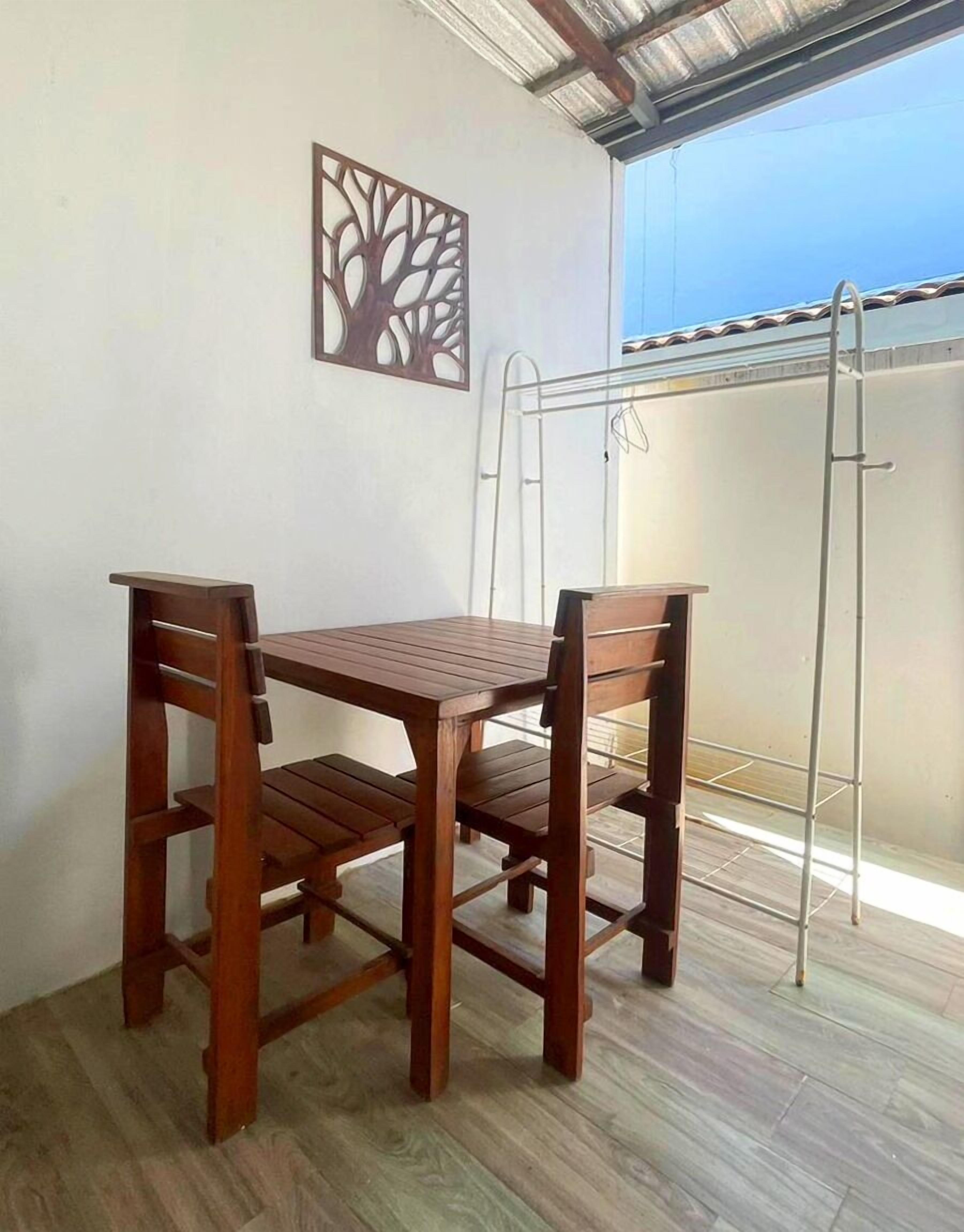 A balcony with a wooden table and chairs, a metal clothes drying rack, and a decorative wall piece.