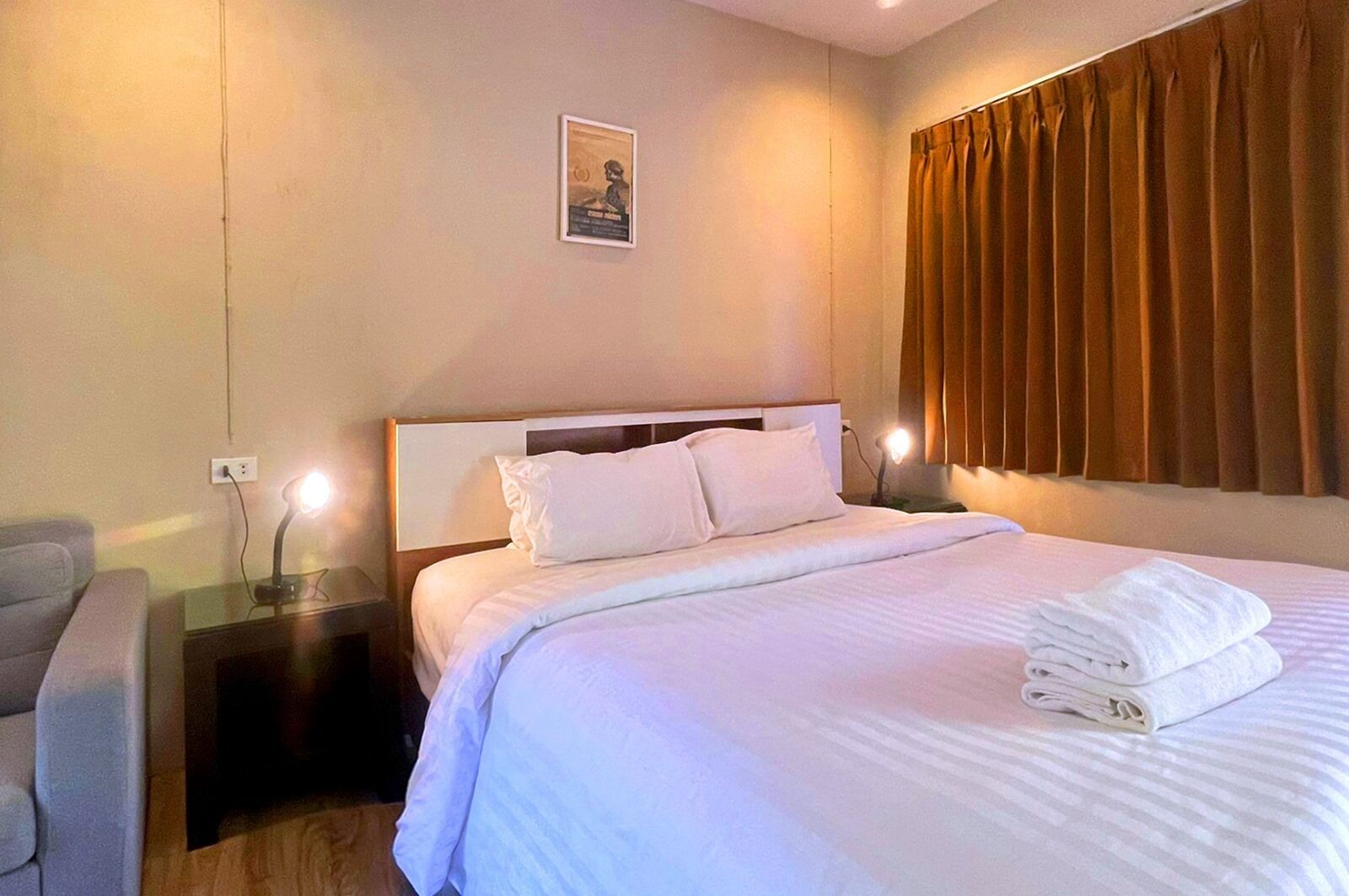 A hotel room with a neatly made bed, a bedside lamp, a chair, and a picture on the wall.
