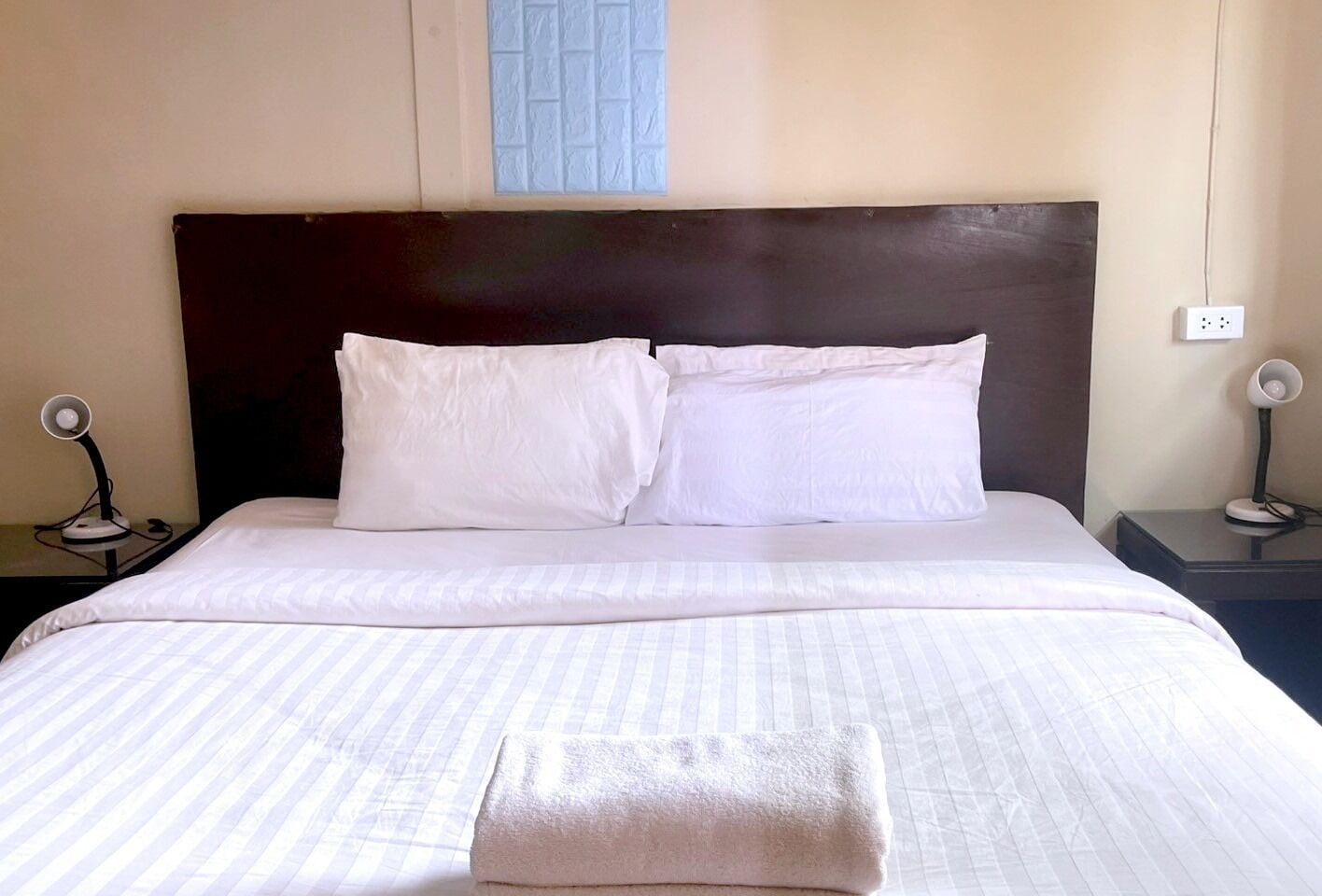 A neatly made bed with white linens and pillows, a dark headboard, and two bedside lamps on either side.