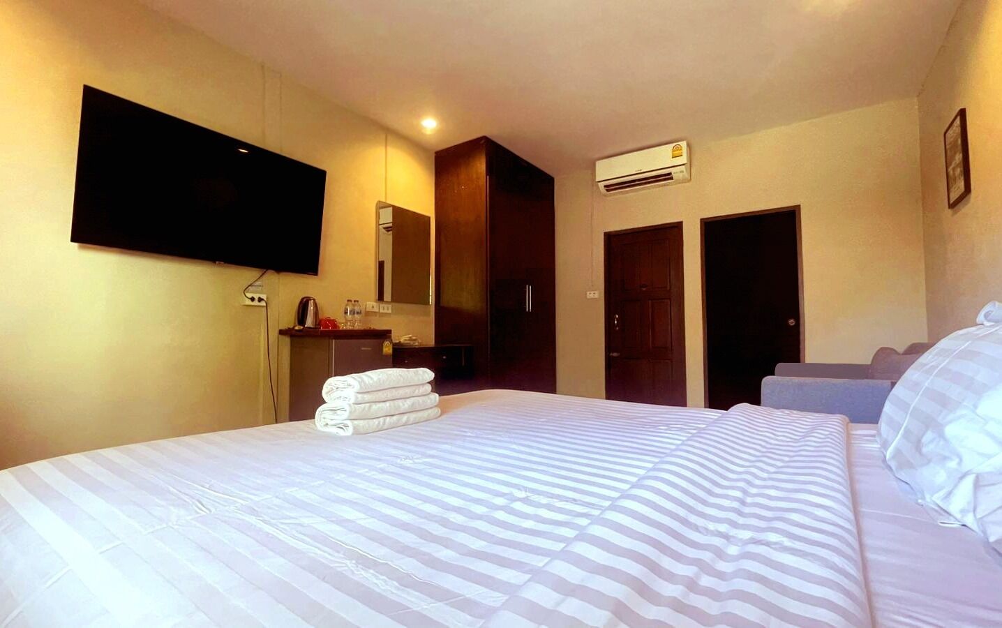 Habitación de hotel con una cama grande, un televisor de pantalla plana montado en la pared, un escritorio con hervidor y un armario.