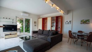 Un saló modern amb un sofà modular, una televisió de pantalla plana, una zona de menjador amb taula i cadires, i una prestatgeria.