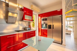 A modern kitchen with red cabinetry, stainless steel appliances, and a glass dining table.