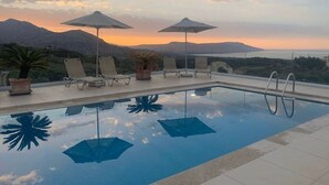 Una piscina infinità amb gandules i ombrel·les, amb les muntanyes de fons durant el capvespre.