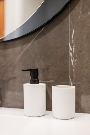A bathroom with a marble wall, a white sink, and a black pump dispenser. - Renovato Deluxe Apartment (Porto)