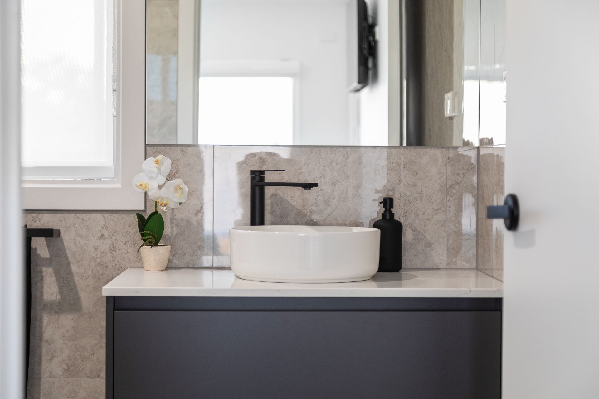 A modern bathroom with a white sink, black faucet, and a potted orchid.