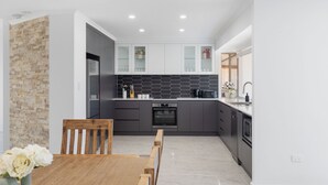 A modern kitchen with grey cabinets, a black tiled backsplash, and a wooden dining table with chairs. - Heinlen on North Terrace  (Mount gambier)