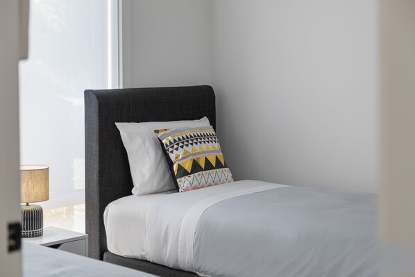 A neatly made bed with a patterned pillow, a bedside lamp, and a window with a view of the outside.