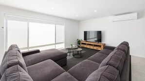 A modern living room with a large grey sofa, a small round table, and a TV on a wooden stand. - Heinlen on North Terrace  (Mount gambier)