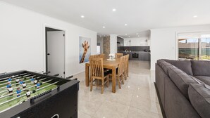A modern living room with a foosball table, a dining area with wooden chairs, and a grey sofa. - Heinlen on North Terrace  (Mount gambier)