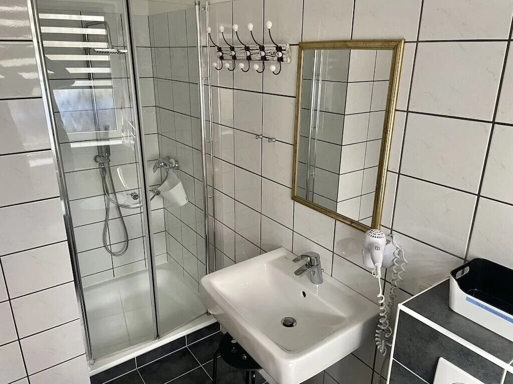 Ett badrum med en dusch som är avskärmad med glasväggar, ett vitt handfat och en spegel med en guldfärgad ram.