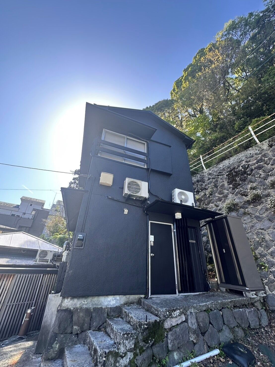 A black building with a stone staircase, a door, and two air conditioning units.