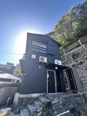 A black building with a stone staircase, a door, and two air conditioning units. - Hakone no Yado (Hakone)